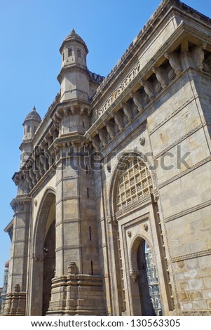 Vertical take of the Gateway of India with a defocused cameo view of the Taj Hotel from an angled view of an archway, vertical shot with clear blue sky