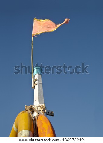 Pink flag flying in the breeze on the mast of a ocean vessel against a rich blue cloudless sky split by yellow life buoys. Generic concept shot location Bet Dwarka, Gujarat, India