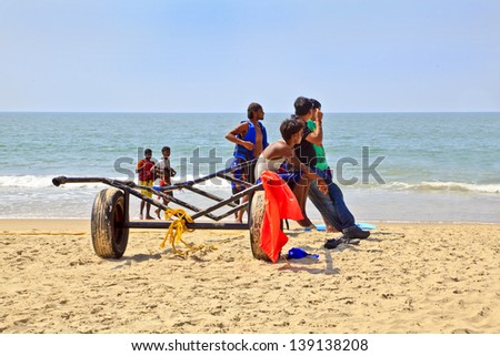 GOA, INDIA - JANUARY 27, 2013: Tropical landscape of paragliding sales assistants sat on trailer waiting for the next fare under the mid day Indian sun on January 27, 2013 in Uttorda Beach, Goa, India