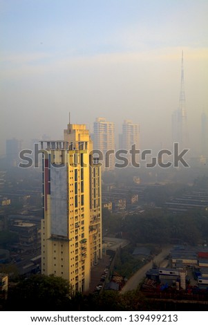 Vertical color capture of Bombay skyline, view osbcured by the city haze and smog in the early hours of the day as the sun rises casting a golden hue over the tall buildings