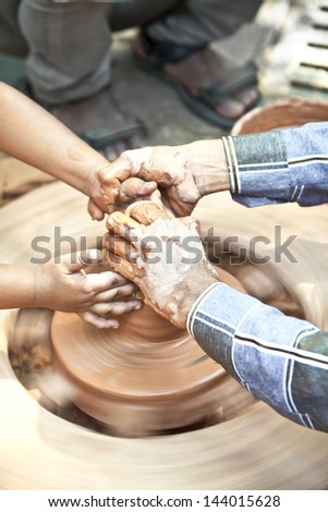 Vertical portrait captured at the Kala Ghoda Festival 2013 held annually in Bombay India, a child being shown how to make a clay pot on a potters wheel by a journeyman providing helping hand to child