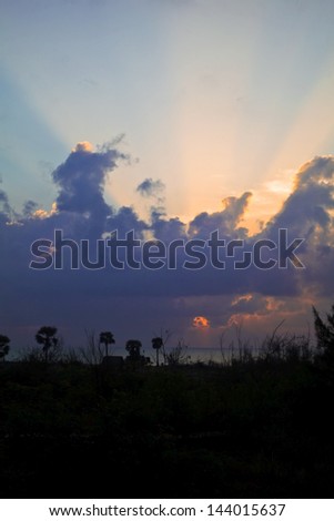 Vertical color portrait of a landscape with the early morning sun peeking through a layer of clouds. Image captured on the coast at Manaputta Beach, Bay of  Bengal with the sun over the horizon line