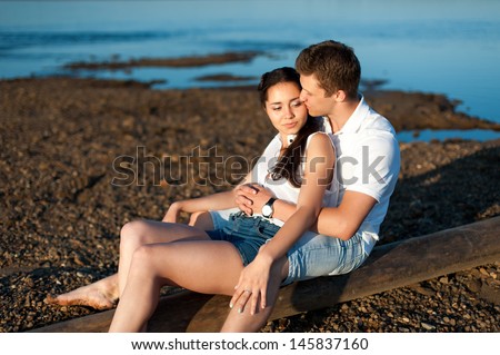 Couple in love walks on the banks of the river in denim shorts and a white shirts.