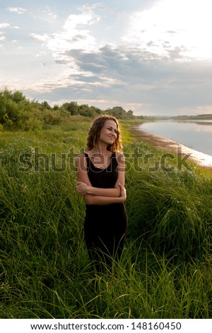 Beautiful girl walks and dreams in high grass on the banks of river