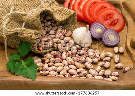 Beans spilled out of the bag with the chopped tomatoes, onions, garlic, pepper and parsley on a wooden board