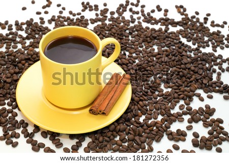Yellow cup of coffee with cinnamon and spilled coffee beans on white background