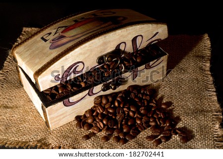 A wooden box filled with coffee beans on  jute table cloth on dim light