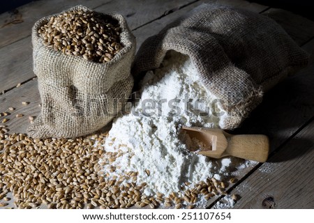 Wheat and Flour in Jute Bags on an Old Wooden Table Over Black Background, Closeup