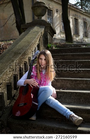 Beautiful Young Blonde Hair Model with Guitar Sitting on the Staircase in the Park on Sunny Spring Day