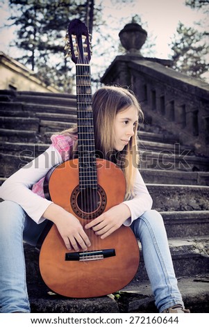 Side View of Thoughtful Young Girl With Guitar in Front of Her Sitting on the Foot of the Stairs and Looking into the Distance