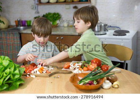 Cute Little Boy Helping His Twin Brother to Make a Fresh Salad at the Kitchen Table at Home