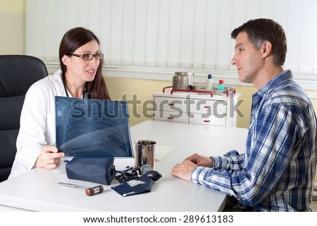 Female Doctor Explaining Lung X-ray Results to Middle Aged Patient in Consulting Room