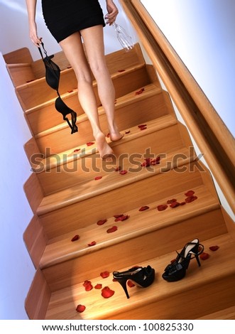 Woman in mini skirt going up the stairs at home, holding bras and glass in hand.