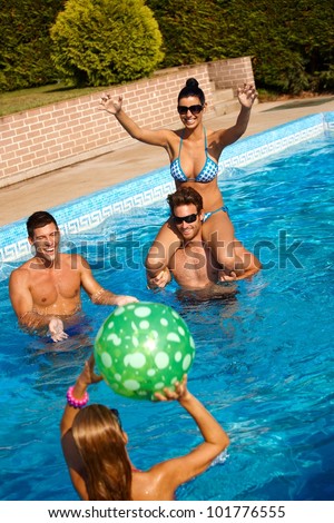 Happy young people playing in swimming pool, having fun.