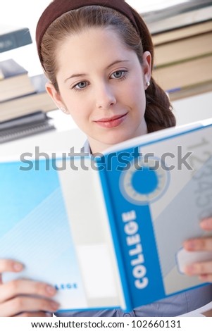 Schoolgirl learning at home, reading exercise book.