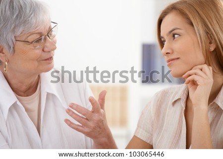 Senior mother and attractive daughter looking at each other with affection, talking, smiling.