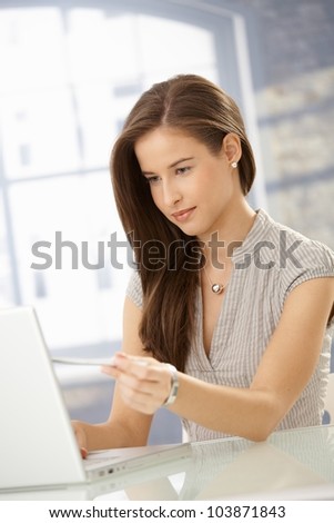 Portrait of attractive young woman sitting at home, using laptop computer, looking at screen.