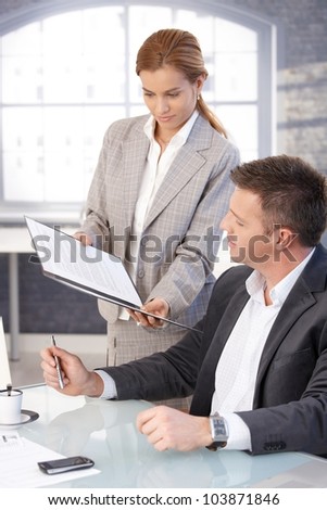Manager sitting at desk, secretary bringing contract to sign.