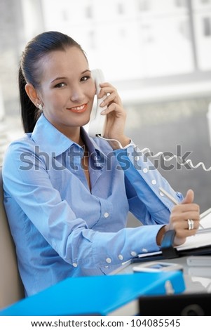 Happy businesswoman speaking on landline phone, smiling at camera.
