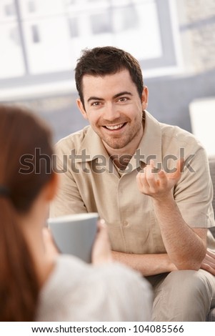 Portrait of happy man chatting with woman at home, sitting in living room.