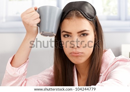 Portrait of tired sleepy woman with coffee mug handheld, wearing sleep mask and pyjama.