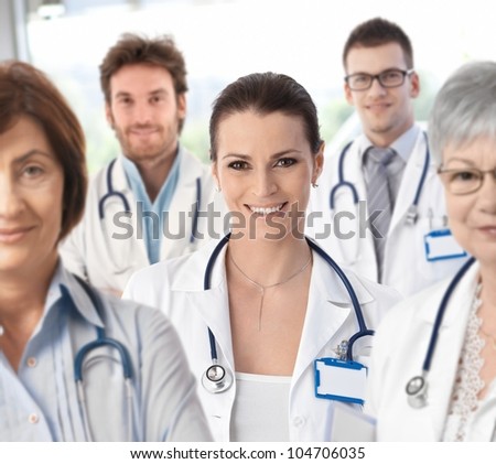 Portrait of female doctor surrounded by medical team, looking at camera, smiling.