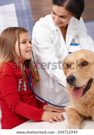 Little girl listening to heartbeat of golden retriever at pets\' clinic, veterinarian examining dog.