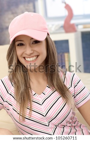 Sporty girl smiling in pink baseball cap at home.