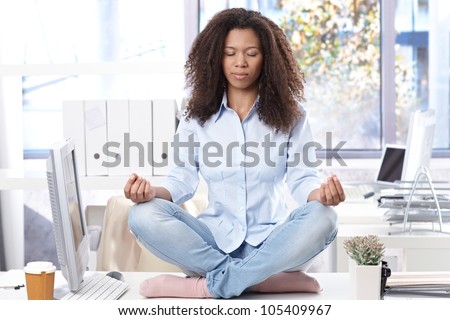Casual ethnic office worker sitting on top of desk, relaxing eyes closed.