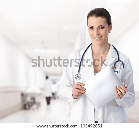 Portrait of woman doctor at hospital corridor, holding tablet computer, looking at camera, smiling.