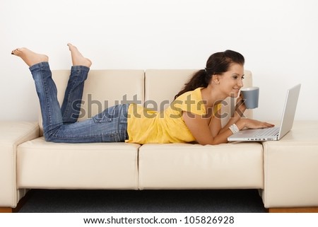 Smiling young girl using laptop computer at home, laying on sofa.