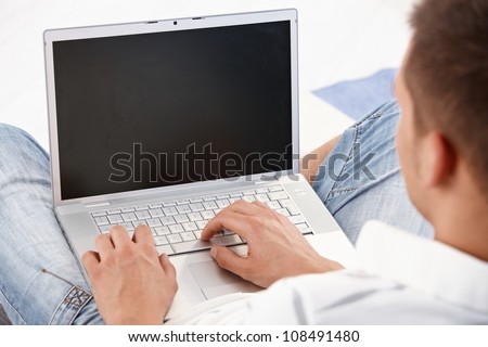 Young man holding laptop in lap, working on it, photographed from behind.