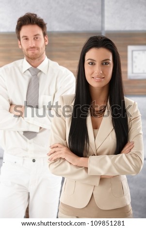 Pretty businesswoman standing arms crossed, smiling, man standing behind.