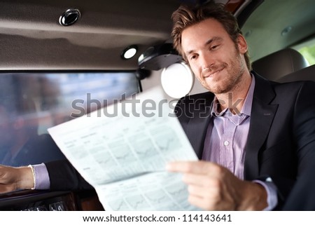 Happy young man reading newspaper in luxury car, smiling.