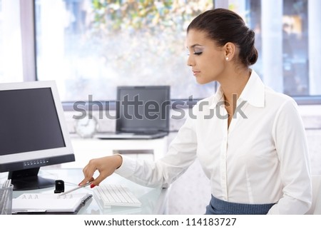 Pretty woman sitting at desk in bright office, looking at organizer, working.