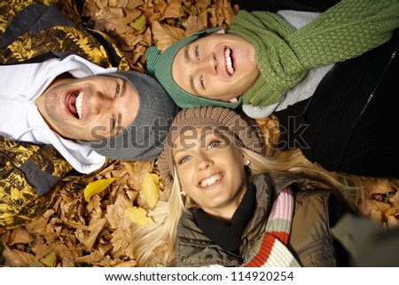 Attractive young people laying on ground among autumn leaves, smiling, having fun.