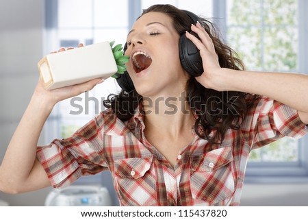 Woman with headphones and imitating using plant as microphone, singing with closed eyes at home.