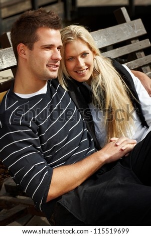Romantic couple sitting on bench, hugging, smiling, enjoying autumn sun.