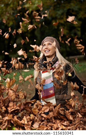 Beautiful young girl having autumn fun in park, smiling, throwing leaves.