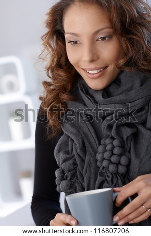 Attractive young smiling woman holding tea mug in hand.
