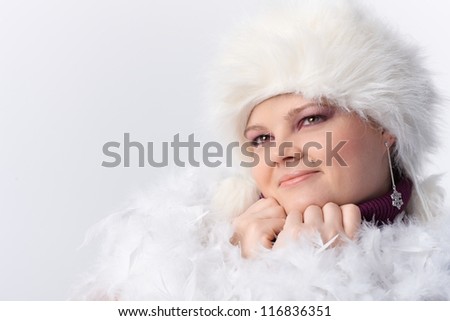 Plump woman smiling among white feathers and fur hat.