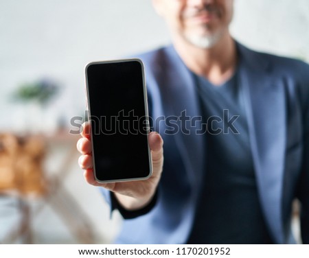 Older white man showing smart phone with blank screen.