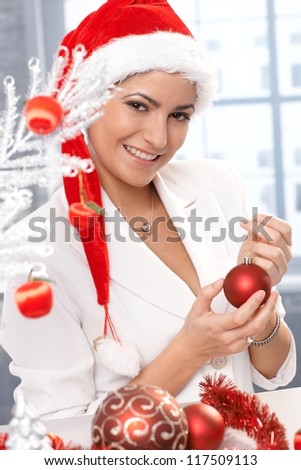 Happy christmas portrait, attractive woman in santa Claus hat smiling, decorating with ornament handheld.
