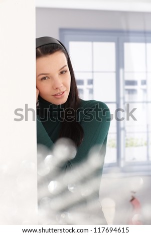 Attractive young woman daydreaming by window, leaning to wall.