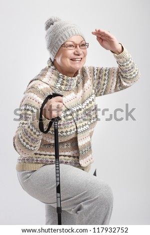 Elderly lady looking to distance, holding hiking poles, smiling.