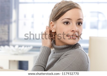 Portrait of young woman, hand in hair, looking away.