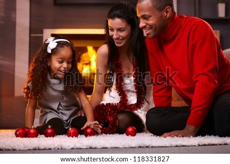 Happy interracial family having fun at home at christmas time, being together, sitting on floor, playing with christmas balls smiling.