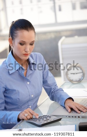 Office worker girl using calculator, busy with financial task at desk.