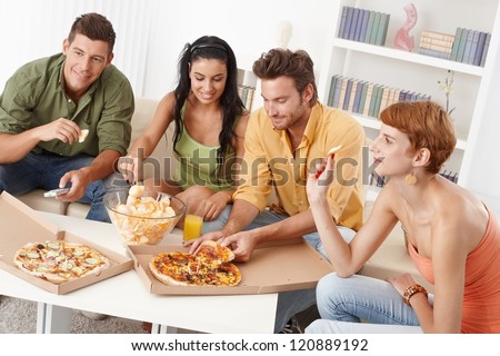 Young friends having party at home, eating pizza and chips, smiling.
