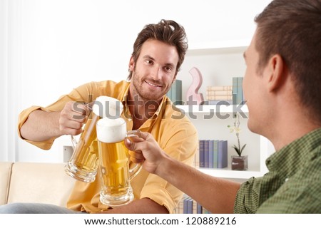 Handsome friends clinking with beer glass, smiling.